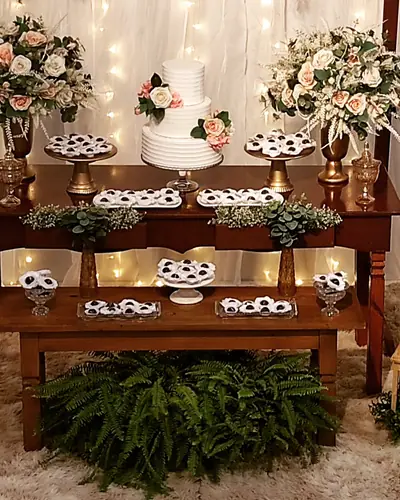 CASAMENTO: mesa de doces rustica de madeira, bolo branco, arranjos de rosas, cortina de luzes. Festa realizada no Espaço Comemora em 2023