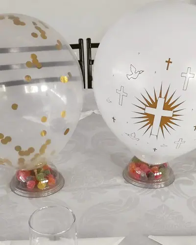 BATIZADO: baloes com cruz e pomba, confete dourado, mesa com toalha branca. Festa realizada no Espaço Comemora em 2023