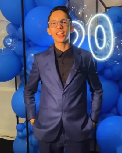 FESTA ADULTA: homem de terno, baloes azuis, neon de numero; legenda fala em Anfitriao. Festa realizada no Espaço Comemora em 2026