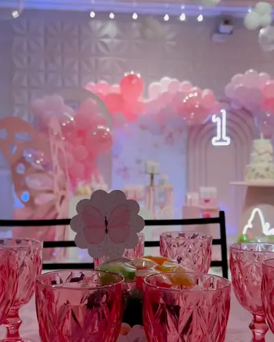 Mesa posta com taças rosa e o salão decorado ao fundo